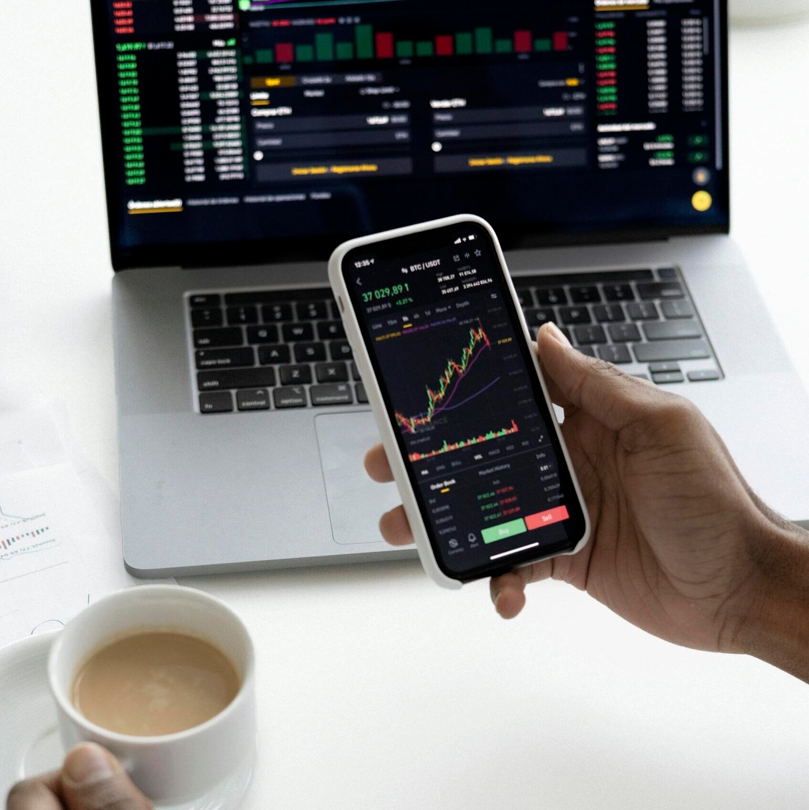 Person analyzing stock market trends on smartphone with laptop background