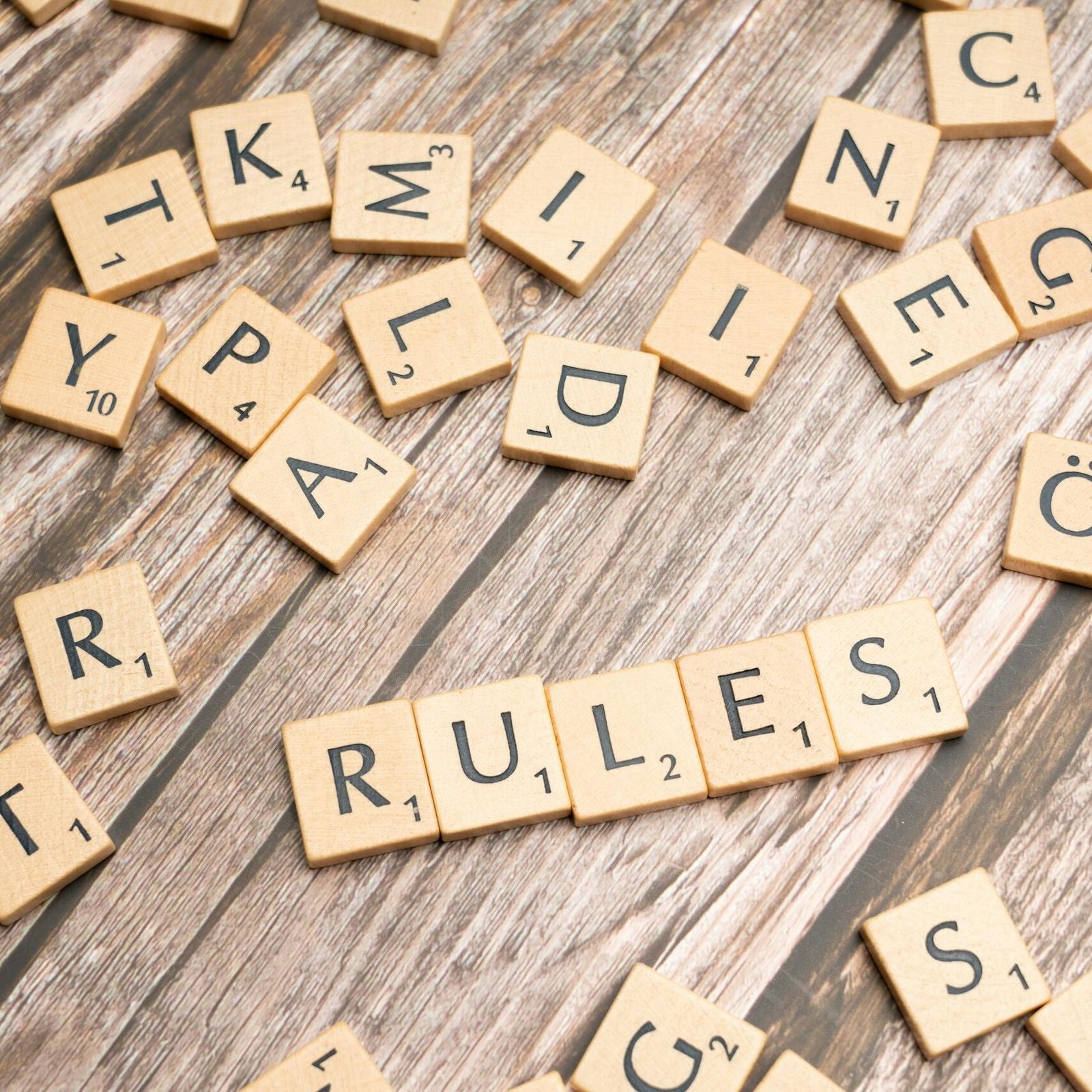 Wooden letter tiles arranged to spell 'Rules' on a textured wooden background.