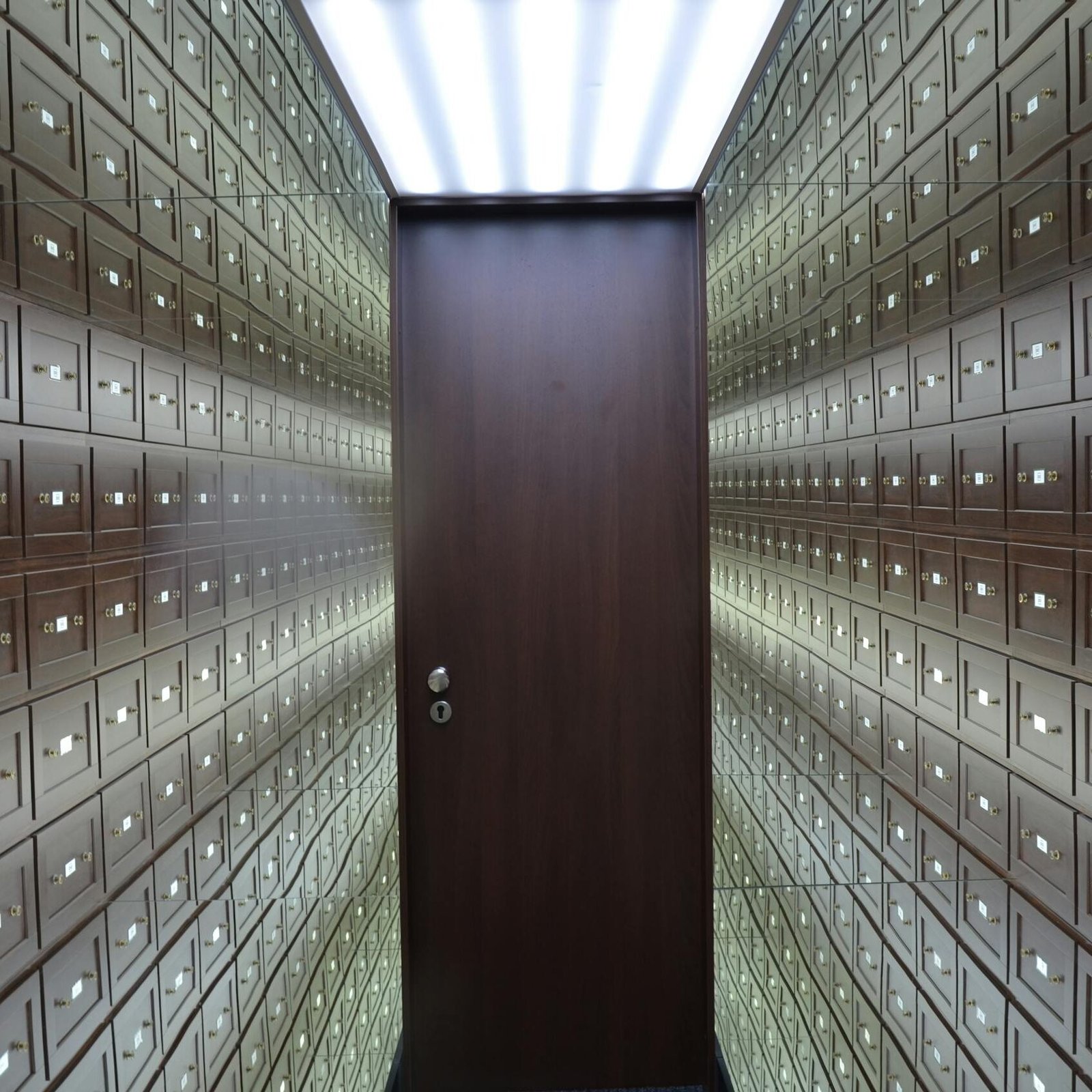 Wooden lockboxes line the walls of a modern, secure vault with a central wooden door.